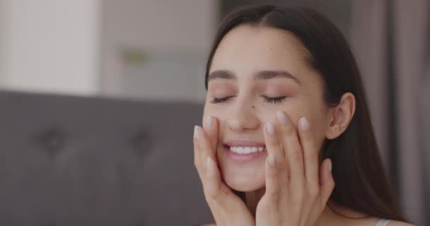 Cuidados de beleza. Close up retrato de alegre mulher do Oriente Médio aplicando creme em suas bochechas, hidratando a pele do rosto — Vídeo de Stock
