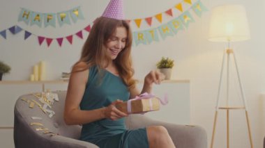Doğum günü hediyesi. Parti şapkalı genç bir kadın hediye kutusunu açıyor, sürpriz koltuğu bekliyor ve gülüyor.