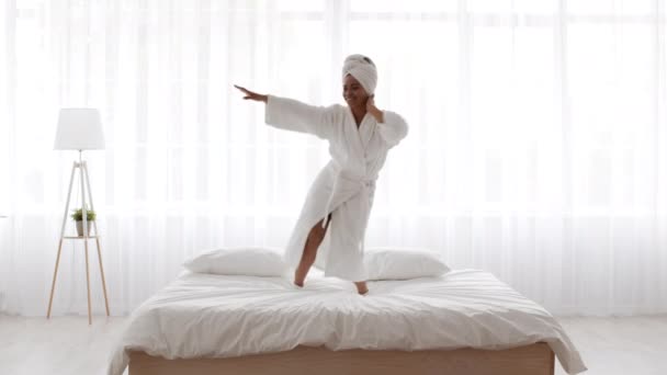 Energieke jong Afrikaans amerikaanse vrouw dragen badjas dansen op bed — Stockvideo