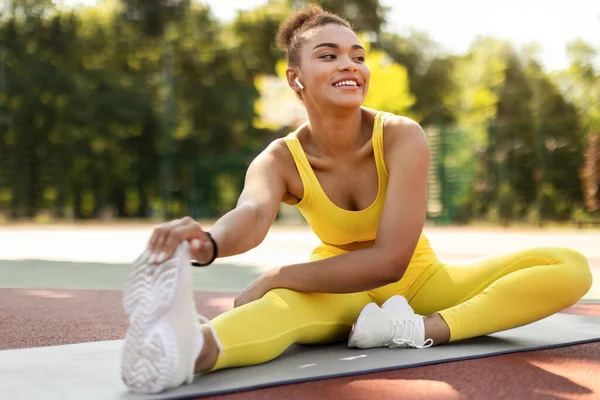 Sonriente negro mujer en amarillo deportivo estiramiento pierna al aire libre — Foto de Stock