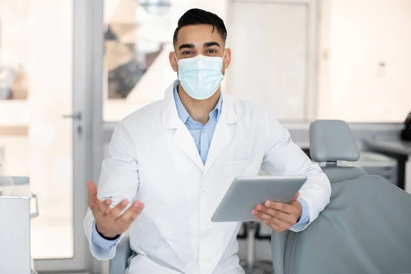 Retrato del guapo dentista árabe en máscara médica usando tableta digital —  Fotos de Stock