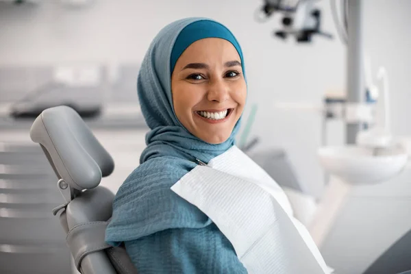 Tratamiento Estomatológico. feliz joven islámica mujer en hiyab sentado en dentistas silla — Foto de Stock