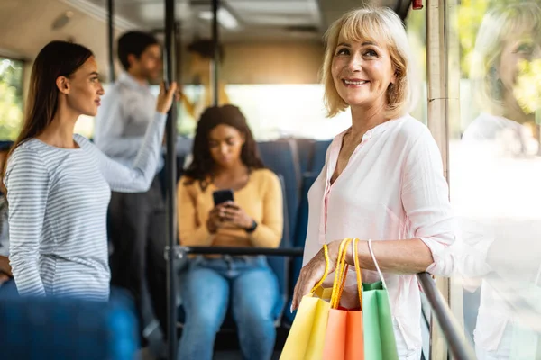 Vacker leende mogen kvinna tar buss, hålla shoppingkassar — Stockfoto