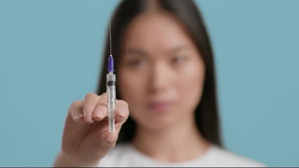 Mulher asiática irreconhecível segurando seringa com vacina antiviral, fundo azul — Vídeo de Stock