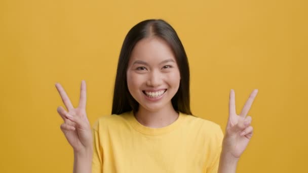 Mulher japonesa Gesturing V-Sign com ambas as mãos sobre fundo amarelo — Vídeo de Stock