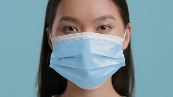 Serious Chinese Lady Wearing Protective Face Mask On Blue Background — Stock Video