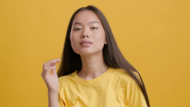 亚洲女人摆弄动人的嘴唇玩头发，黄色背景 — 图库视频影像