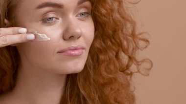 Kızıl Saçlı Kadın Bej Arkaplanda Yüz Kremi Kullanıyor