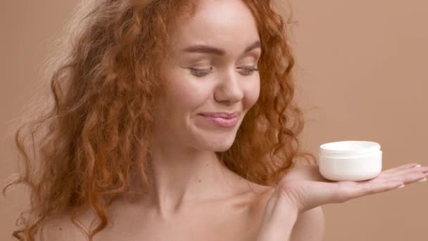 Happy Ginger-Haired Lady segurando hidratante creme frasco sobre fundo bege — Vídeo de Stock