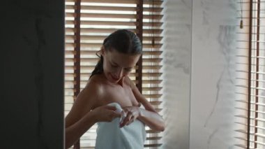 Duştan sonra banyoda duran beyaz havluyu saran çekici kadın.