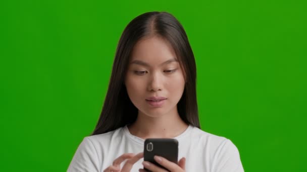 Emozionato asiatico donna utilizzando smartphone celebrando grandi notizie, sfondo verde — Video Stock