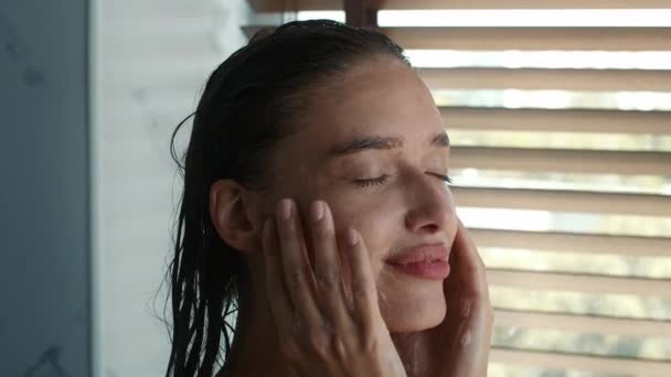Жінка доглядає за обличчям приймає душ, роблячи масаж обличчя індору — стокове відео
