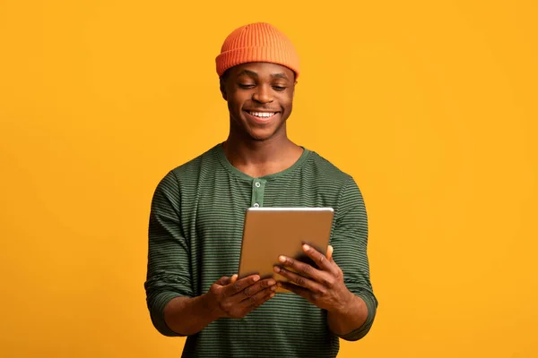 Retrato de un joven afroamericano sonriente usando una tableta digital, fondo amarillo —  Fotos de Stock