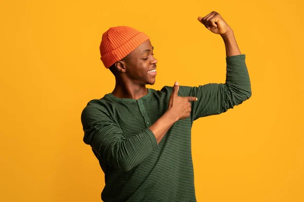 Feliz jovem afro-americano cara apontando para seus bíceps enquanto bombeando punho — Fotografia de Stock