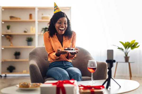Siyahi kadın akıllı telefonun önünde doğum günü pastası tutuyor. — Stok fotoğraf