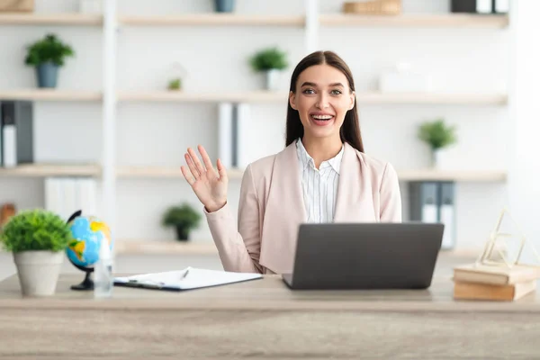 Vrolijke vrouwelijke manager zwaaien Hallo zittend op laptop in Office — Stockfoto