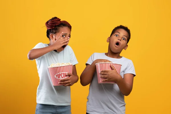 Skrämd afro-amerikan pojke och flicka med popcorn buskets tittar på skräck — Stockfoto