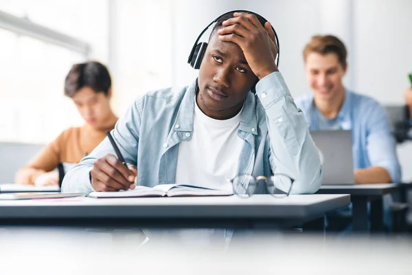 Zwarte mannelijke student die zit te schrijven aan het bureau in de klas — Stockfoto