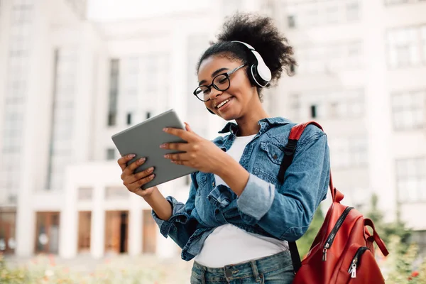 Estudiante negra feliz usando la computadora de la tableta que usa auriculares afuera —  Fotos de Stock