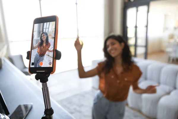 Jeune influenceuse enregistrant du contenu vidéo, dansant à la caméra à la maison, mise au point sélective du smartphone sur trépied — Photo