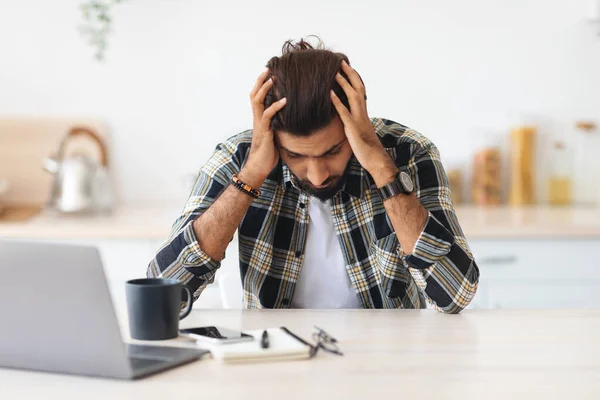 沮丧的男人坐在笔记本电脑前，摸着自己的头 — 图库照片