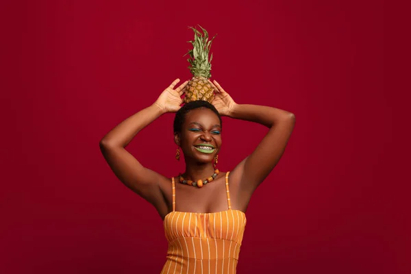 Feliz mujer negra sosteniendo piña en la cabeza y riendo — Foto de Stock