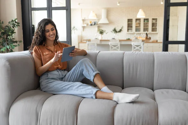 Millennial signora utilizzando tablet pc, studiare o lavorare in remoto, avendo conferenza online, seduto sul divano a casa — Foto Stock