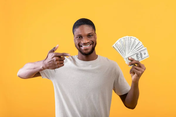 Gran suerte financiera y concepto de ganancias. Hombre afroamericano sosteniendo dinero, señalándolo con el dedo, fondo amarillo — Foto de Stock