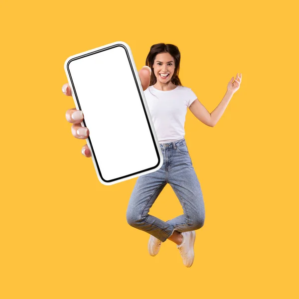 Frau zeigt weißen leeren Smartphone-Bildschirm und springt auf — Stockfoto
