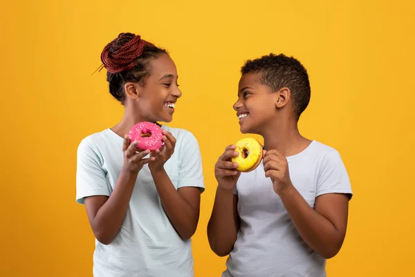 Vrolijke zwarte jongen en meisje eten heerlijke donuts — Stockfoto