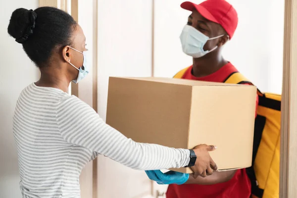 Deliveryman In Face Mask Giving Box für weibliche Kunden in Innenräumen — Stockfoto