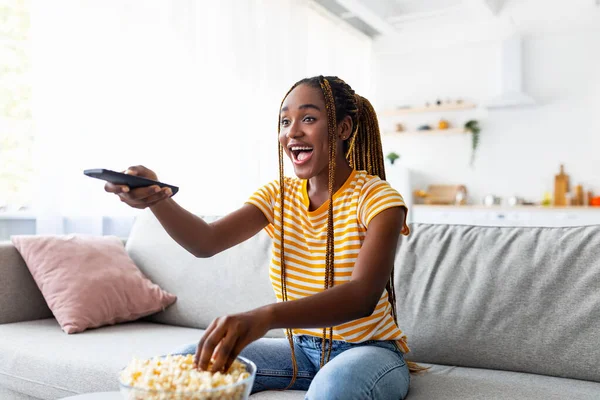 Śmiejąca się afro amerykańska młoda kobieta oglądająca telewizję w domu — Zdjęcie stockowe