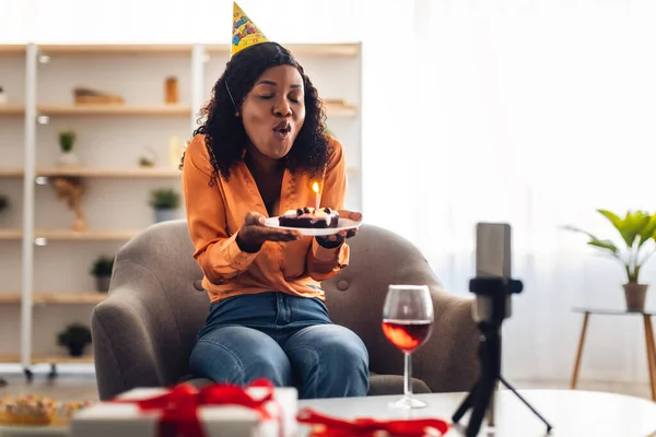 Femme africaine soufflant la bougie sur le gâteau d'anniversaire au téléphone portable à l'intérieur — Photo