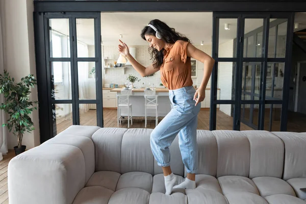 Evde müzik dinlerken koltukta dans eden, kulaklıklı, pozitif genç bir kadın. — Stok fotoğraf