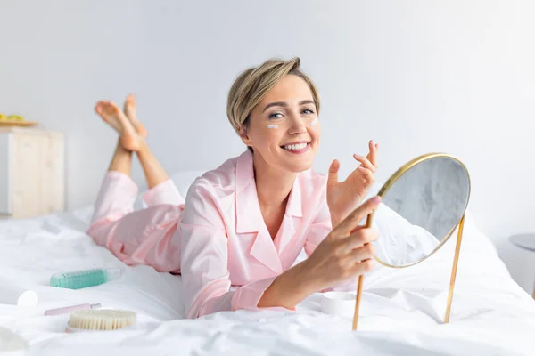 Retrato de mujer sonriente sosteniendo espejo aplicando crema — Foto de Stock