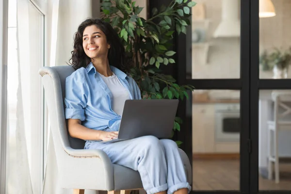 Mulher milenar feliz sentado em poltrona com computador portátil, trabalhando ou estudando em casa, espaço de cópia — Fotografia de Stock