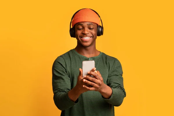 Vidám afro-amerikai srác használ okostelefon és zenét hallgat vezeték nélküli fejhallgató — Stock Fotó