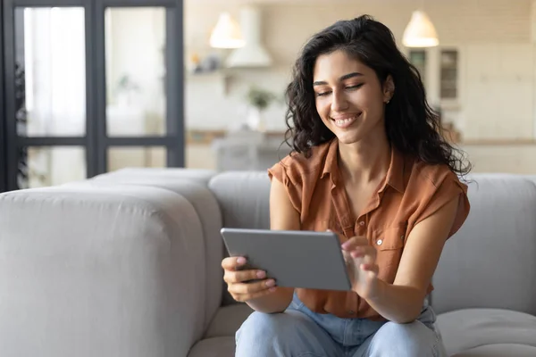 Portret van een lachende jonge vrouw met een tablet, thuis op de bank, kopieerruimte — Stockfoto