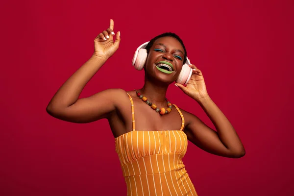 Senhora negra despreocupada ouvindo música, usando fones de ouvido sem fio — Fotografia de Stock