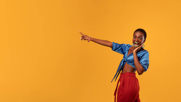Surprised african american stylish millennial woman in glamorous summer outfit with bright makeup pointing aside, showing copy space for text or advertisement, panorama with empty space