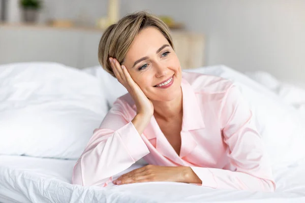 Mujer madura feliz mirando hacia otro lado y pensando en la cama — Foto de Stock