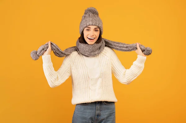 Moda de inverno cocnept. positivo jovem mulher vestindo camisola quente, cinza tricotado chapéu e cachecol, fundo laranja — Fotografia de Stock