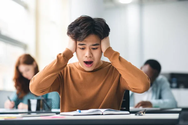 Shocked asiático estudiante agarrando cabeza sentado en escritorio en clase — Foto de Stock