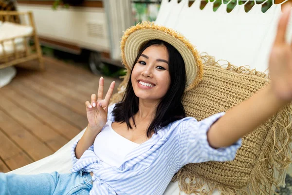 Feliz joven asiática mujer tomando selfie mientras que miente en hamaca cerca de RV en vacaciones del otoño en campo — Foto de Stock