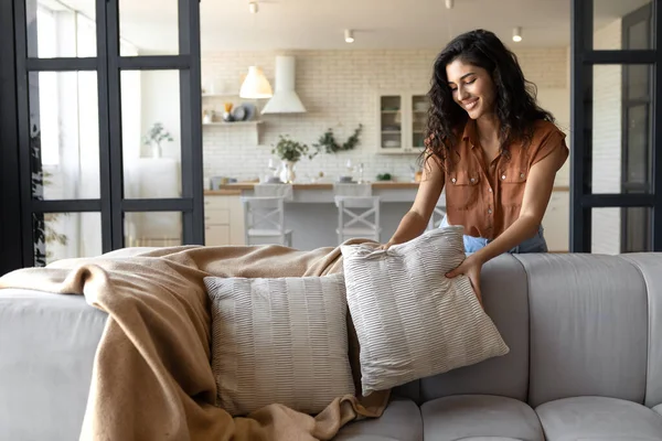 Härlig ung kvinna sätta mjuka kuddar och rutig på bekväm soffa, vilket gör hennes hem mysig och varm, kopiera utrymme — Stockfoto