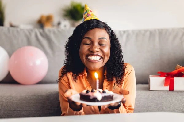 Černá žena dělat přání foukání svíčka na narozeniny dort vnitřní — Stock fotografie