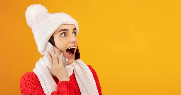 Wow aanbod. Verrast dame in de winter outfit praten op smartphone en kijken naar vrije ruimte op gele achtergrond — Stockfoto