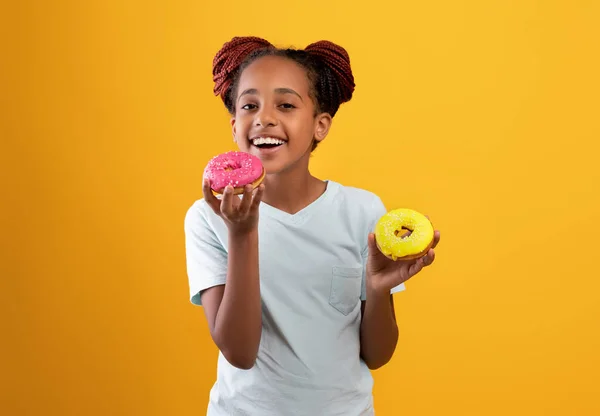 Mooi zwart meisje met kleurrijke donuts, geïsoleerd op gele achtergrond — Stockfoto