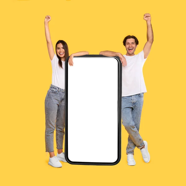 Couple showing white empty smartphone screen and making win gesture — Stock Photo, Image