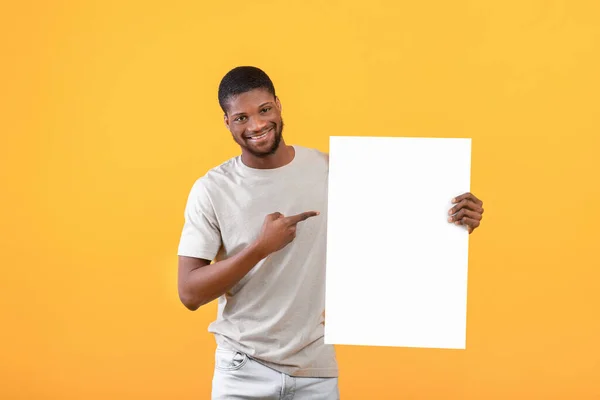 Freiraum für Werbung. Aufgeregter schwarzer Mann zeigt auf leeres Poster mit Mockup für Ihr Design, gelber Hintergrund — Stockfoto